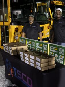 Larry Franklin and Stanley Woods standing at a table handing out subway meal kits after a football game