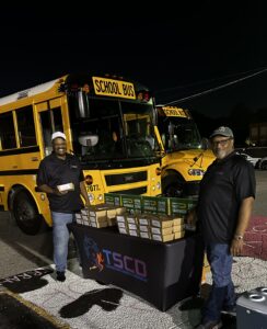 Larry Franklin and Stanley Woods standing at a table handing out subway meal kits after a football game